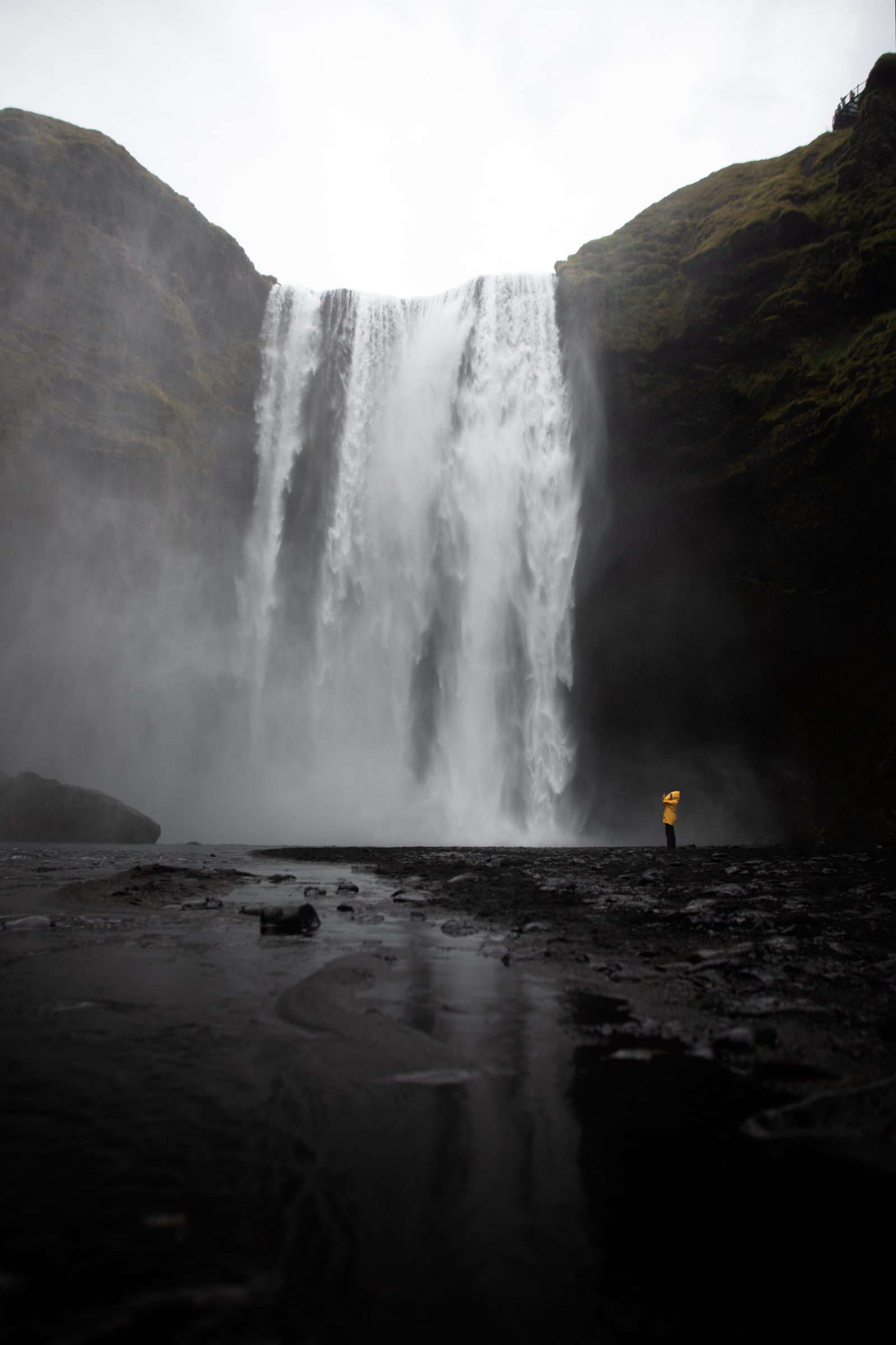 A single figure in a yellow coat dwarfed by Skógafoss waterfall