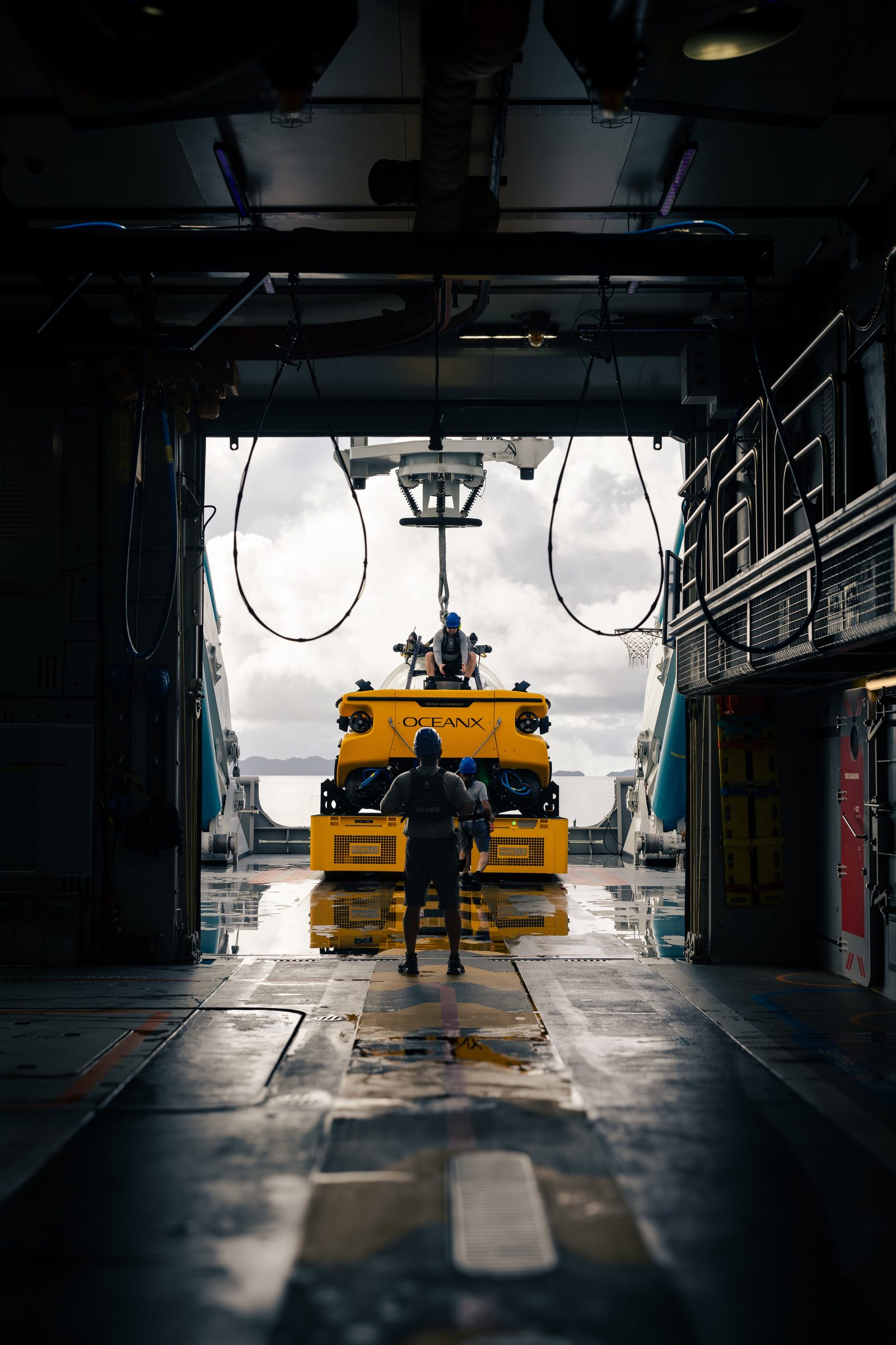 OceanX submersible being lowered into the hangar bay, crew watching